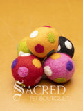 A pile of colourful wool felt balls with polka dots sits on a wooden table. Suitable for all cats and small to teacup sized dogs.