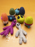 A collection of colorful felt cat toys with various shapes and patterns that have the theme of outer space. Included are spaceships, alien faces and alien figures. Displayed on a wooden background with a white Sacred Pet Boutique