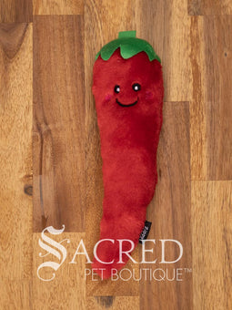 A red furry chilli pepper cat toy with a happy smiling face and a green top or hat sits on a wooden surface.