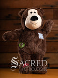 Brown Wild Knot teddy bear dog toy with a white face and black nose, wearing a 'Sacred Pet Boutique' tag, on a wooden background.