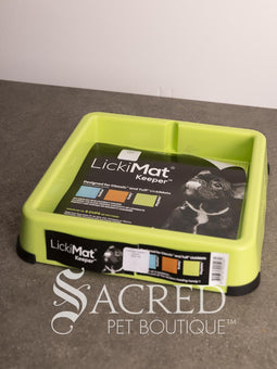 A light blue LickiMat Keeper pet lick mat tray with its retail packaging insert, placed on a gray countertop against a white wall. A watermark for 'Sacred Pet Boutique' is visible at the bottom.