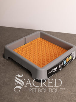 A light blue LickiMat Keeper pet lick mat tray with its retail packaging insert, placed on a gray countertop against a white wall. A watermark for 'Sacred Pet Boutique' is visible at the bottom.