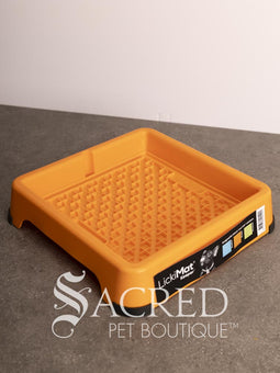 A light blue LickiMat Keeper pet lick mat tray with its retail packaging insert, placed on a gray countertop against a white wall. A watermark for 'Sacred Pet Boutique' is visible at the bottom.