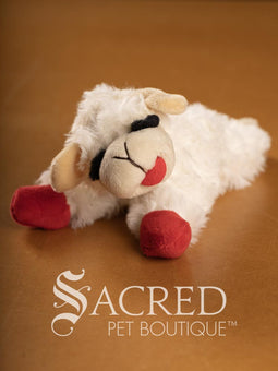 Two plush Lamb Chop sheep dog toys with red feet and tongues on a wooden surface, branded 'Sacred Pet Boutique'.