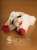 Plush Lamb Chop squeaky dog toy with closed eyes on a brown surface, branded as Sacred Pet Boutique.