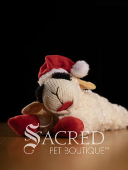 Plush toy sheep with a Santa hat on a dark background, featuring the Sacred Pet Boutique logo.