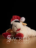 Plush toy sheep with a Santa hat on a dark background, featuring the Sacred Pet Boutique logo.