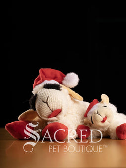 Plush toy sheep with a Santa hat on a dark background, featuring the Sacred Pet Boutique logo.