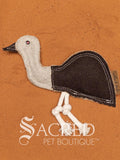 Ernie the Emu is a wool felt dog toy with multiple rows of stitching, on a wooden background. A white Sacred Pet Boutique watermark.