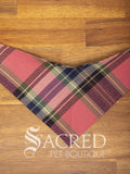 A pink Plaid tartan dog bandana on a wooden table with 'Sacred Pet Boutique' branding.
