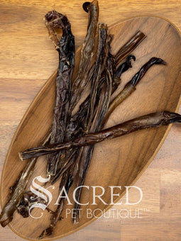 A wooden plate containing dried pork chews for dogs. On a wooden background, with a white Sacred Pet Boutique watermark.