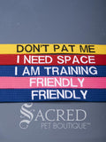 A group of dog collars and leashes with embroidered safety messages in white or black. On a grey background with a Sacred Peet Boutique watermark.