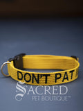 A bright yellow dog collar with embroidered safety message "Don't Pat Me" in black. With a steel D-ring and black plastic side release clip. On a grey background with a Sacred Peet Boutique watermark.