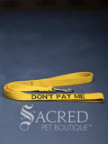 A bright yellow dog leash with embroidered safety message "Don't Pat Me" in black. With a steel snap hook. On a grey background with a Sacred Peet Boutique watermark.