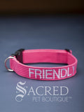 A Bright Pink dog collar with embroidered safety message "Friendly" in white. With a steel D-ring and black plastic side release clip. On a grey background with a Sacred Peet Boutique watermark.