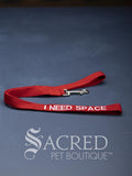 A Bright Red dog leash with embroidered safety message "I Need Space" in white. With a steel snap hook. On a grey background with a Sacred Peet Boutique watermark.