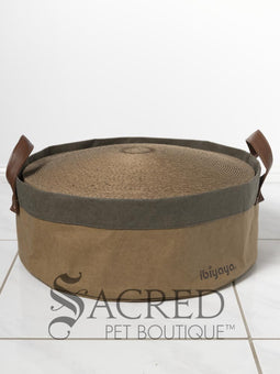 A Chinchilla Persian cat scratching the top of a brown cardboard cat scratcher in front of a white wall with a white 'Sacred Pet Boutique' watermark