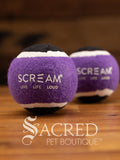 A set of two purple and black medium tennis ball sits on a wooden table with a wooden background. The ball is solid foam, so it won't pop, has dog friendly fuzz and does not squeak.