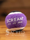 A single purple and black small tennis ball sits on a wooden table with a wooden background. The ball is solid foam, so it won't pop, has dog friendly fuzz and does not squeak.