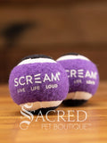 A set of two purple and black small tennis balls sit on a wooden table with a wooden background. The ball is solid foam, so it won't pop, has dog friendly fuzz and does not squeak.