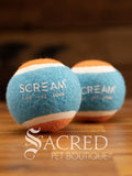 A set of two blue and orange medium tennis balls sit on a wooden table with a wooden background. The ball is solid foam, so it won't pop, has dog friendly fuzz and does not squeak.