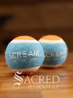 A single blue and orange tennis ball sits on a wooden table with a wooden background. The ball is solid foam, so it won't pop, has dog friendly fuzz and does not squeak.