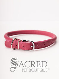 A black, round, soft leather dog collar with a metal buckle clasp. Our beautiful Soft Round (Rolled) leather collars are highly recommended for long haired dogs. Round or rolled collars reduce the amount of matting, tangling and flattening of the dogs fur. All collars are hand made and stitched with wax thread, from the finest quality soft leather wrapped and stitched around a nylon inner cord for added strength.Image on a white background, with the Sacred Pet Boutique logo.