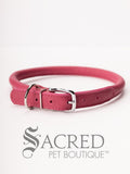 A pink, round, soft leather dog collar with a metal buckle clasp. Our beautiful Soft Round (Rolled) leather collars are highly recommended for long haired dogs. Round or rolled collars reduce the amount of matting, tangling and flattening of the dogs fur. All collars are hand made and stitched with wax thread, from the finest quality soft leather wrapped and stitched around a nylon inner cord for added strength.Image on a white background, with the Sacred Pet Boutique watermark.