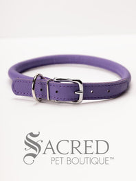 A black, round, soft leather dog collar with a metal buckle clasp. Our beautiful Soft Round (Rolled) leather collars are highly recommended for long haired dogs. Round or rolled collars reduce the amount of matting, tangling and flattening of the dogs fur. All collars are hand made and stitched with wax thread, from the finest quality soft leather wrapped and stitched around a nylon inner cord for added strength.Image on a white background, with the Sacred Pet Boutique logo.