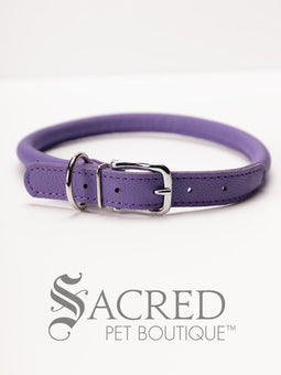 A black, round, soft leather dog collar with a metal buckle clasp. Our beautiful Soft Round (Rolled) leather collars are highly recommended for long haired dogs. Round or rolled collars reduce the amount of matting, tangling and flattening of the dogs fur. All collars are hand made and stitched with wax thread, from the finest quality soft leather wrapped and stitched around a nylon inner cord for added strength.Image on a white background, with the Sacred Pet Boutique logo.