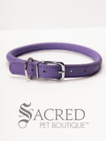 A purple, round, soft leather dog collar with a metal buckle clasp. Our beautiful Soft Round (Rolled) leather collars are highly recommended for long haired dogs. Round or rolled collars reduce the amount of matting, tangling and flattening of the dogs fur. All collars are hand made and stitched with wax thread, from the finest quality soft leather wrapped and stitched around a nylon inner cord for added strength.Image on a white background, with the Sacred Pet Boutique watermark.