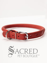 A black, round, soft leather dog collar with a metal buckle clasp. Our beautiful Soft Round (Rolled) leather collars are highly recommended for long haired dogs. Round or rolled collars reduce the amount of matting, tangling and flattening of the dogs fur. All collars are hand made and stitched with wax thread, from the finest quality soft leather wrapped and stitched around a nylon inner cord for added strength.Image on a white background, with the Sacred Pet Boutique logo.