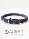 A purple, round, soft leather dog collar with a metal buckle clasp. Our beautiful Soft Round (Rolled) leather collars are highly recommended for long haired dogs. Round or rolled collars reduce the amount of matting, tangling and flattening of the dogs fur. All collars are hand made and stitched with wax thread, from the finest quality soft leather wrapped and stitched around a nylon inner cord for added strength.Image on a white background, with the Sacred Pet Boutique watermark.