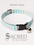 An aqua and white striped soft fabric cat collar with black plastic hardware and a silver bell with a safety breakaway buckle on a white background. A Sacred Pet Boutique watermark