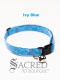 A Blue Ivy patterned soft fabric cat collar with black plastic hardware and a silver bell with a safety breakaway buckle on a white background. A Sacred Pet Boutique watermark.