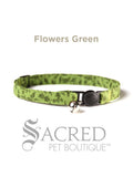 A green floral patterned soft fabric cat collar with black plastic hardware and a silver bell with a safety breakaway buckle on a white background. A Sacred Pet Boutique watermark.