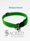 An green striped soft fabric cat collar with black plastic hardware and a silver bell with a safety breakaway buckle on a white background. A Sacred Pet Boutique watermark