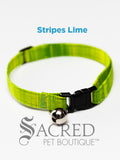 An green striped soft fabric cat collar with black plastic hardware and a silver bell with a safety breakaway buckle on a white background. A Sacred Pet Boutique watermark