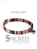 An red white brown pink cream striped soft fabric cat collar with black plastic hardware and a silver bell with a safety breakaway buckle on a white background. A Sacred Pet Boutique watermark