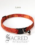 A red lava patterned soft fabric cat collar with black plastic hardware and a silver bell with a safety breakaway buckle on a white background. A Sacred Pet Boutique watermark.