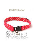 A red Polka Dot soft fabric cat collar with black plastic hardware and a silver bell with a safety breakaway buckle on a white background. A Sacred Pet Boutique watermark.
