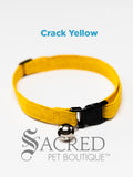 A Yellow Crack Patterned soft fabric cat collar with black plastic hardware and a silver bell with a safety breakaway buckle on a white background. A Sacred Pet Boutique watermark.