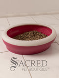 A pink Vicci litter tray in a white room on a white tiled floor. It is filled with kitty litter.