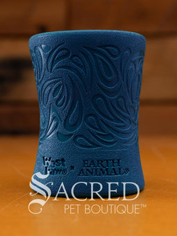 A green, funnel-shaped dog treat dispenser with an intricate carved paisley swirl pattern and the surface has a distinct, finely pebbled texture. At the base of the toy there is the West Paw brand and the words EARTH ANIMAL embossed in it. It is sitting on a wood surface with a wooden background and with a white Sacred Pet Boutique watermark. 