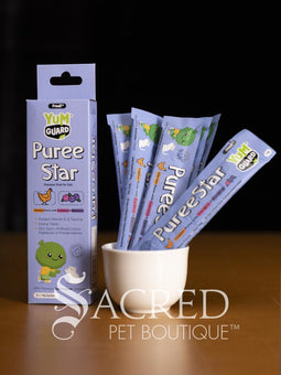 Four Yumguard Puree Star pet treats in different flavours (Fish and Mango, Chicken and Papaya, Fish and Apple, Chicken and berries) in colourful packaging, displayed on a wooden surface against a black background. With a white Sacred Pet Boutique watermark.
