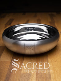A beautifully styled curved sided double walled steel bowl with brand name ZEEZ etched on the outer brushed finished edge shows the highly polished inner where the brand name is embossed on the base. Place on a wooden table and watermarked with Sacred Pet Boutique