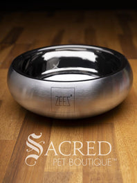 A beautifully styled curved sided double walled steel bowl with brand name ZEEZ etched on the outer brushed finished edge shows the highly polished inner where the brand name is embossed on the base. Place on a wooden table and watermarked with Sacred Pet Boutique