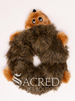 A plush dog toy resembling a wolf in a neutral grey colour, placed on a flat surface, with the brand 'Sacred Pet Boutique' visible.