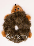 A plush dog toy resembling a hedgehog in brown colours, placed on a flat surface, with the brand 'Sacred Pet Boutique' visible.