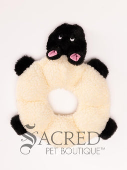A plush dog toy resembling a wolf in a neutral grey colour, placed on a flat surface, with the brand 'Sacred Pet Boutique' visible.